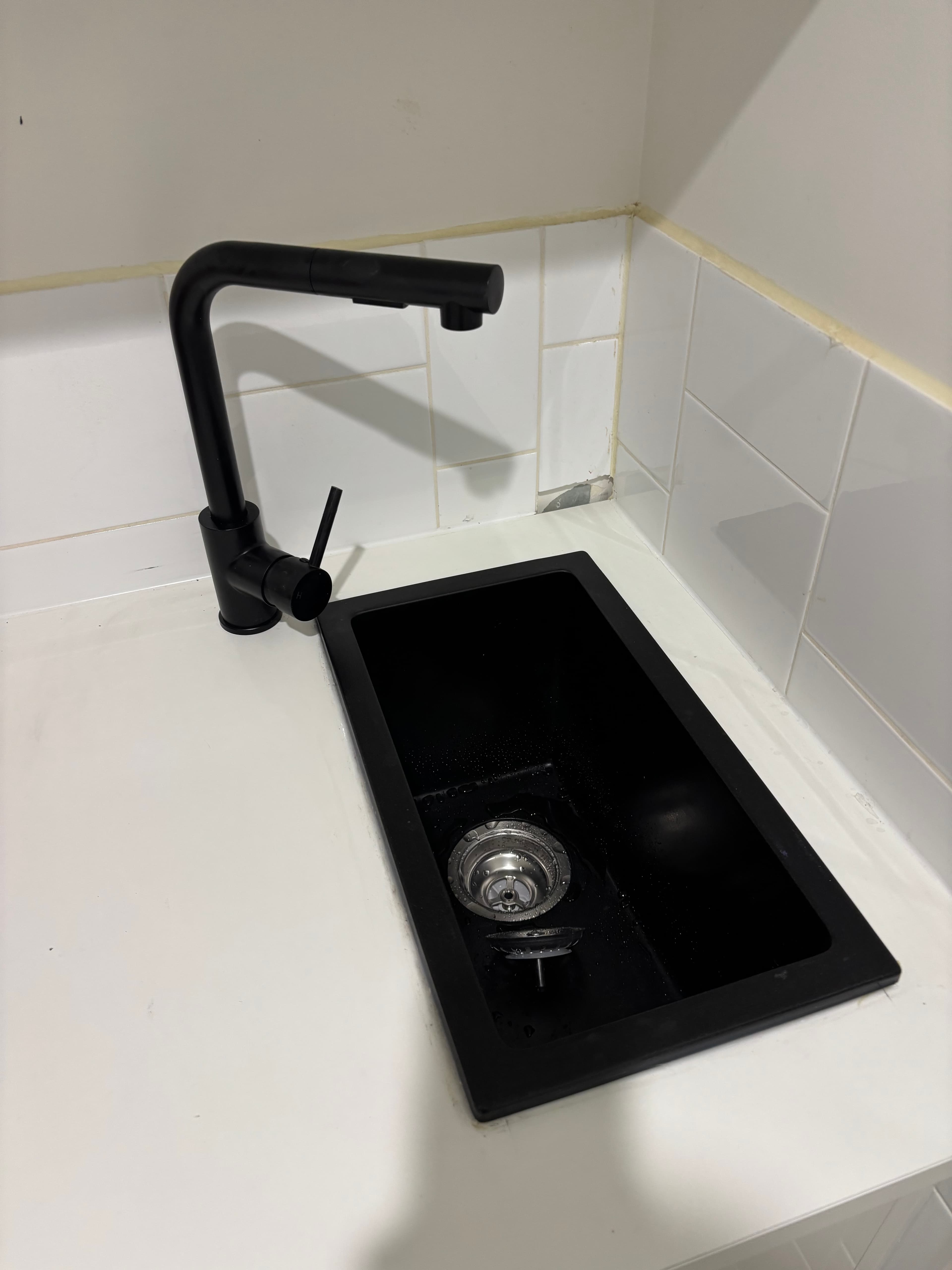 Sleek black faucet and matching rectangular sink installed in a white countertop with tiled backsplash.