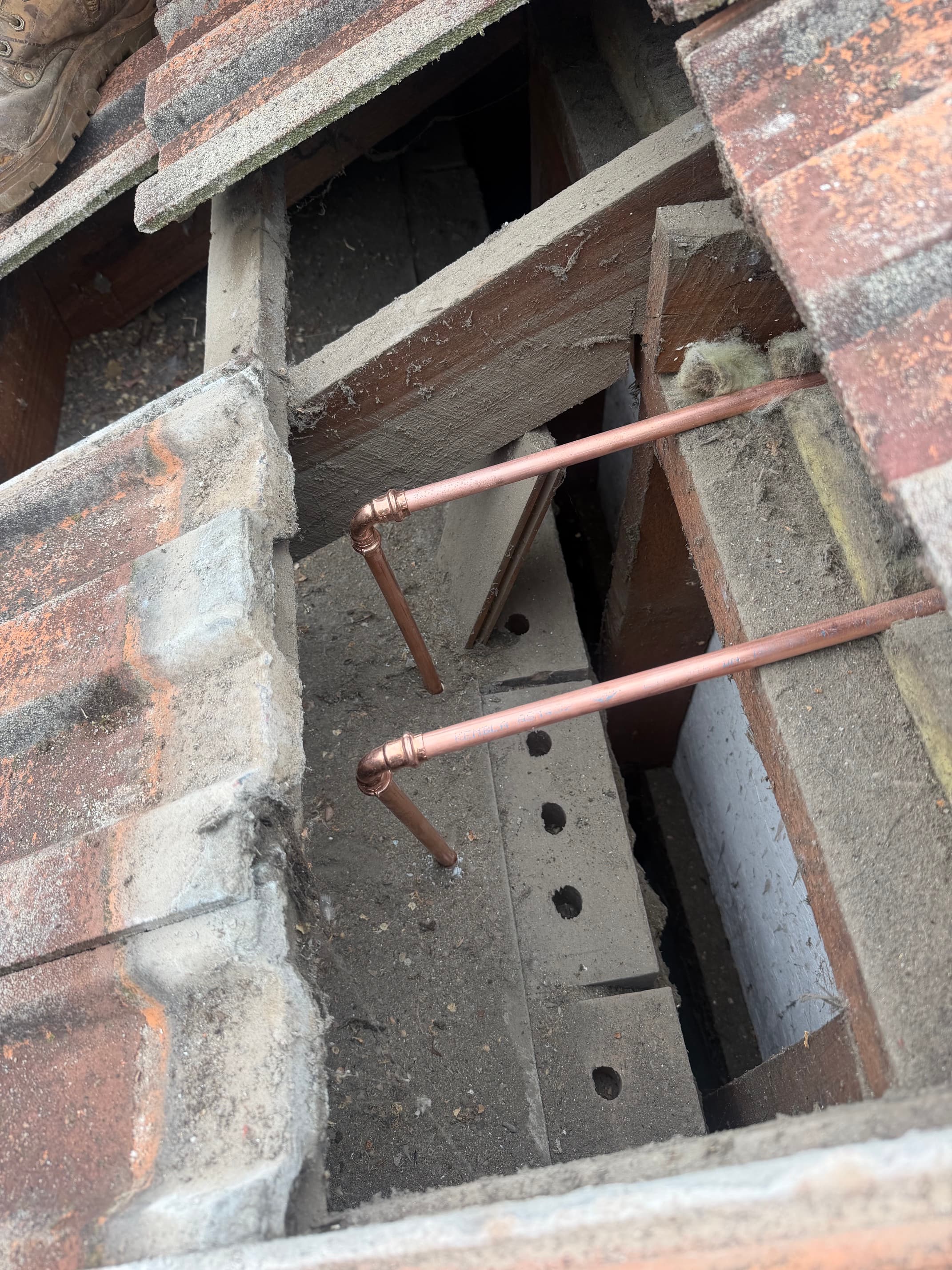 Two copper pipes with elbow joints installed beneath a partially removed tiled roof structure.