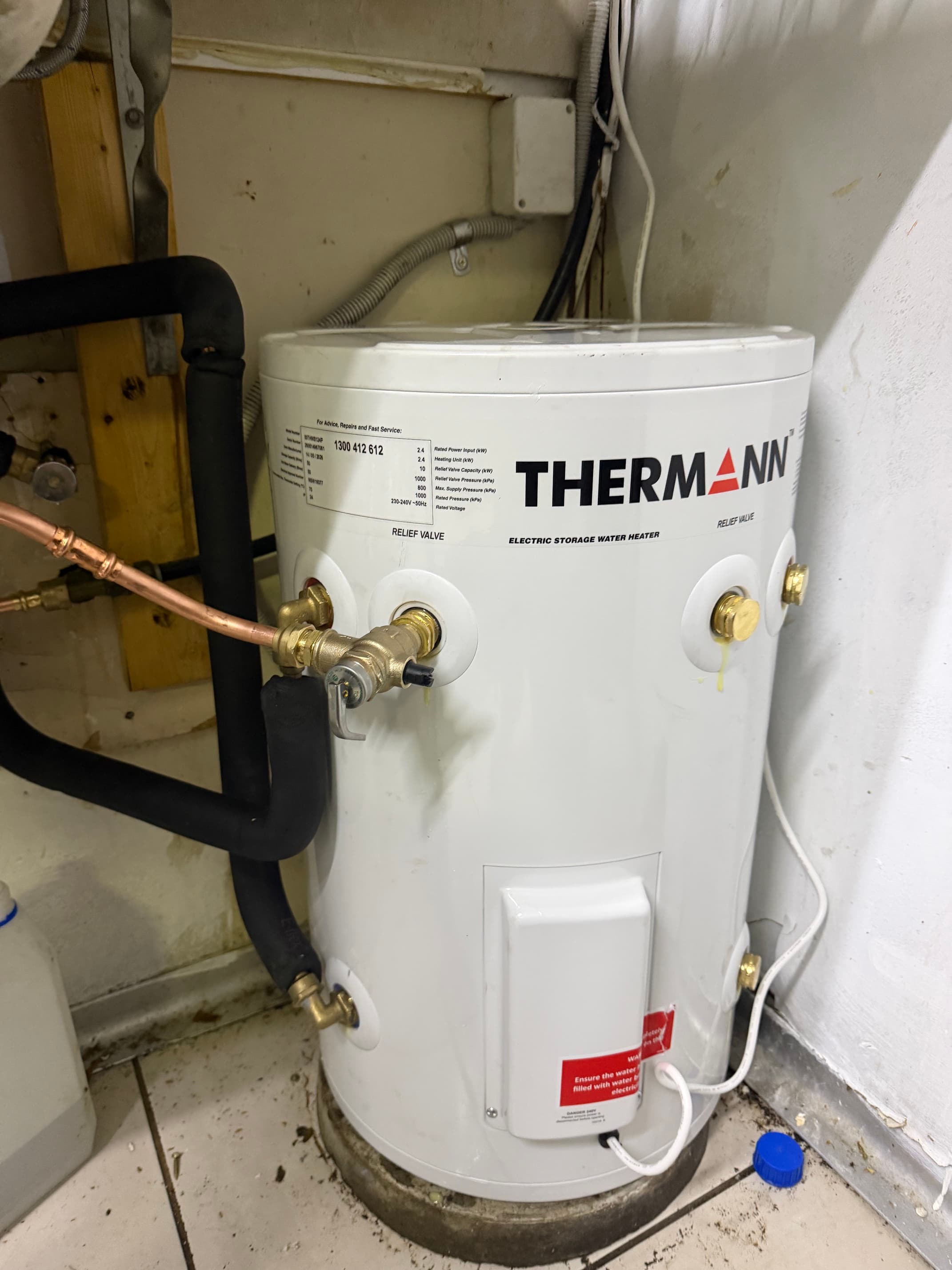 White Thermann electric storage water heater connected to copper pipes and black insulated tubing.