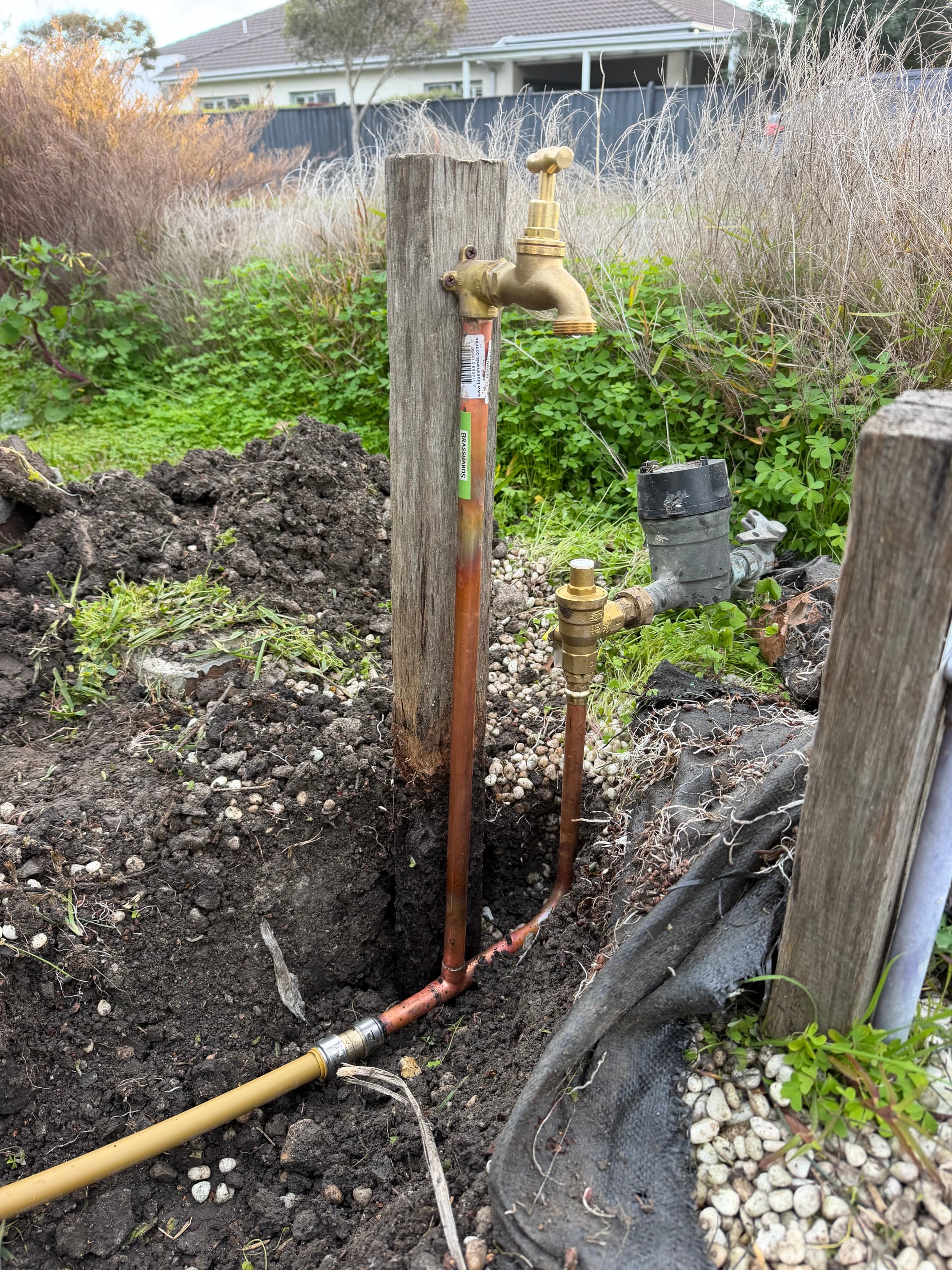 Brass outdoor tap on a wooden post with copper pipes and an exposed water meter.